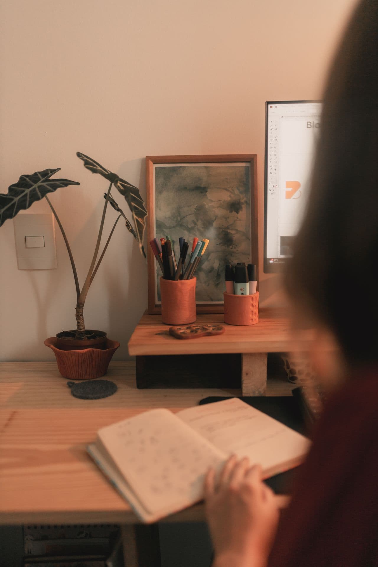 A calm workspace with a desk, notebook, and plant in warm light.